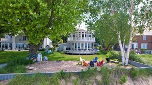 Ein ans Wasser gebautes Anwesen mit einer überdachten Terrasse, Sitzgelegenheiten im Freien und einer Sandfläche zum Entspannen.