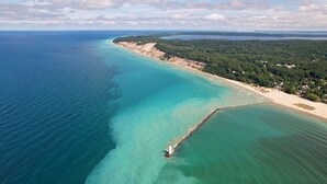 Eine Vogelperspektive auf eine Küstenlandschaft mit einem Leuchtturm, klarem türkisblauem Wasser und einem Sandstrand.