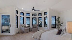 Ein Schlafzimmer mit einem großen Bett, zwei Sesseln, einem Deckenventilator und mehreren Fenstern mit Blick ins Freie.