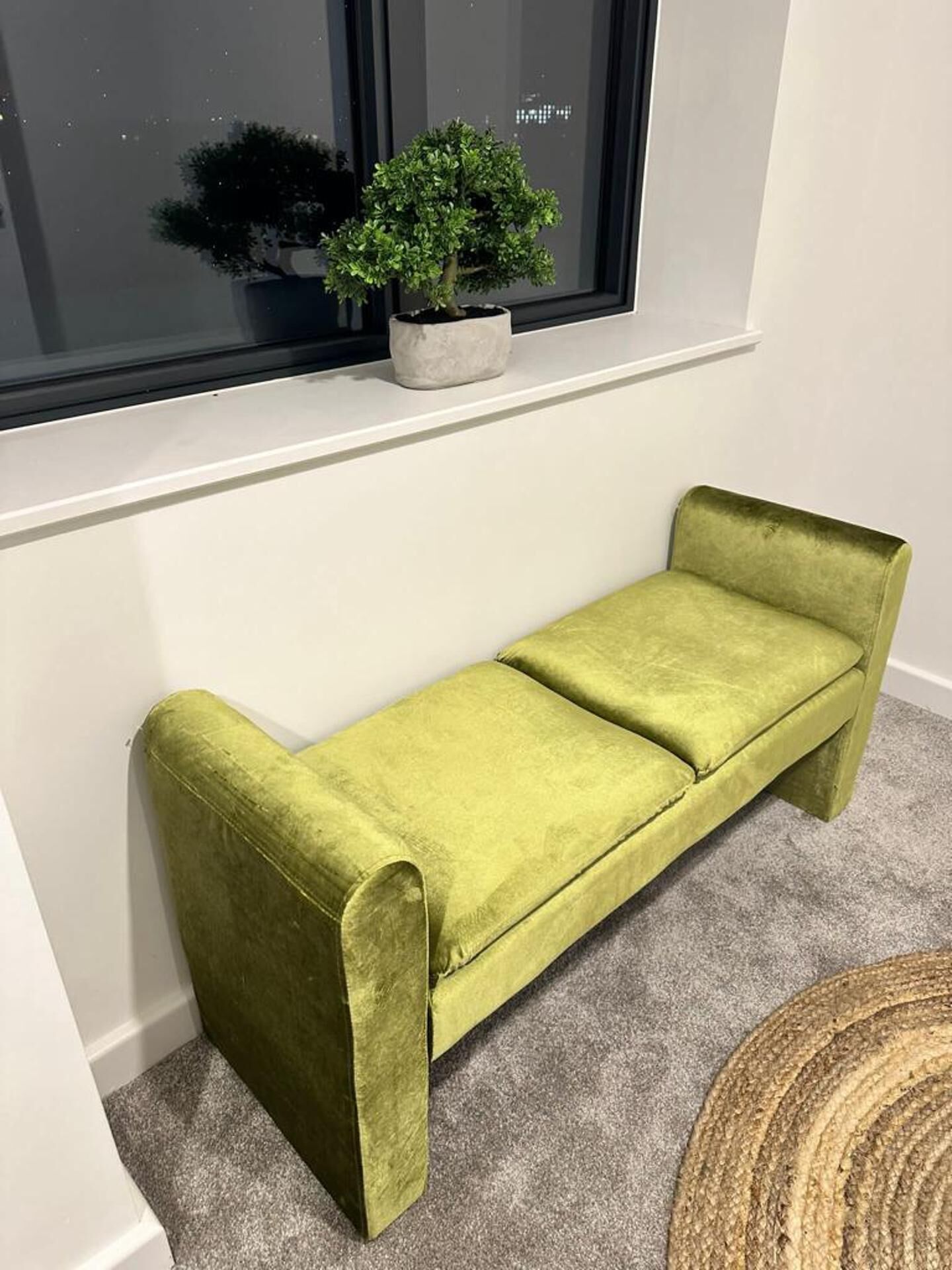 A green bench with a potted plant on a windowsill.