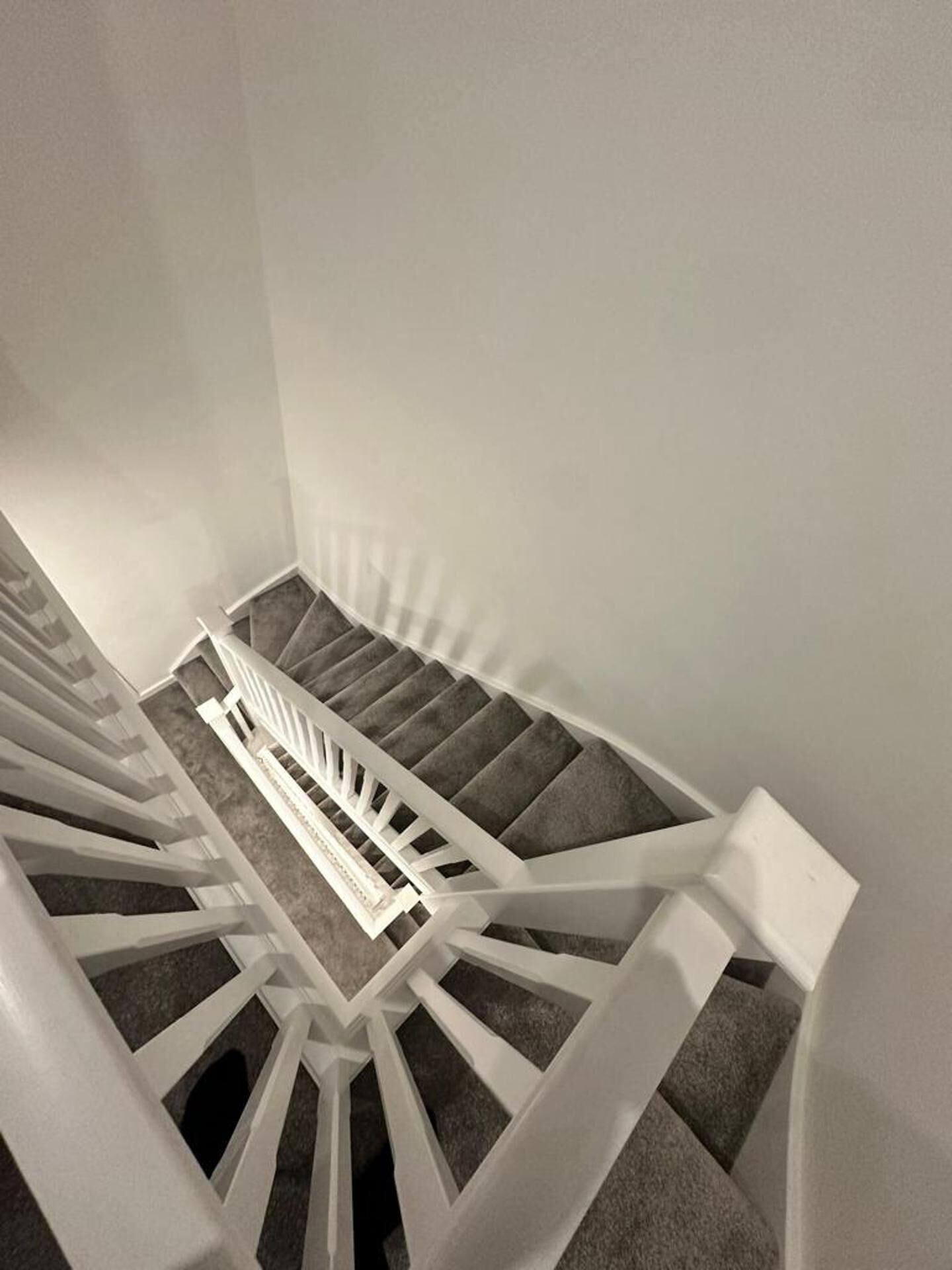 Eine Wendeltreppe mit weißen Geländern und grauen Teppichstufen.
