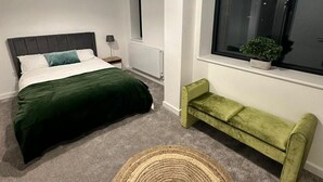 Un dormitorio moderno con cama, un banco, un ventanal grande y una lámpara de techo.