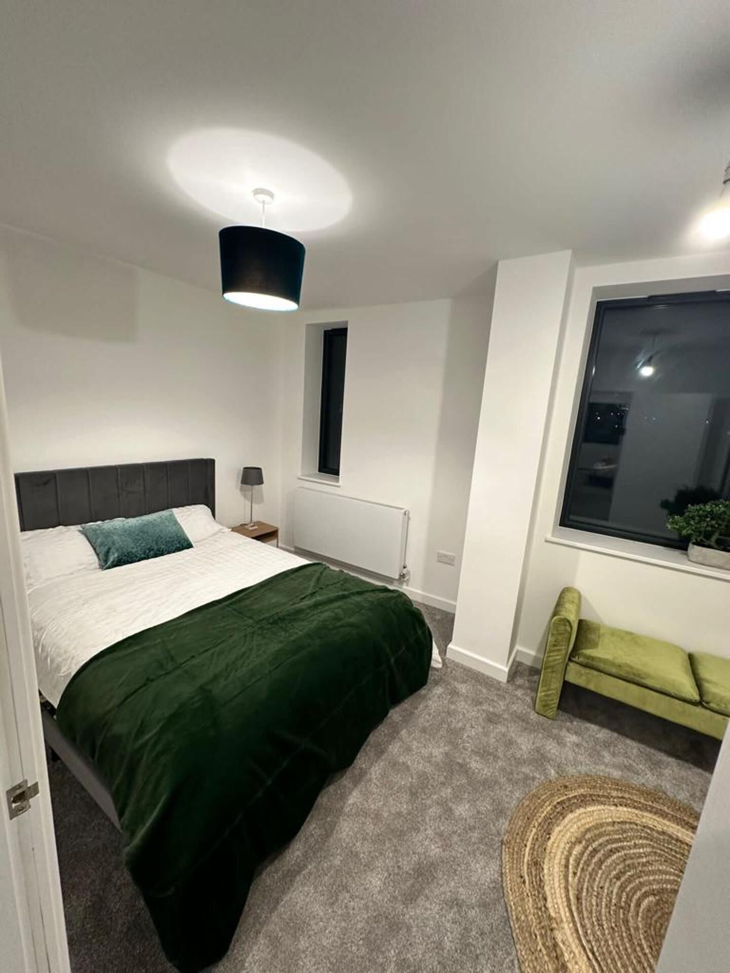 A bedroom with a bed, a window, a radiator, and a green bench.