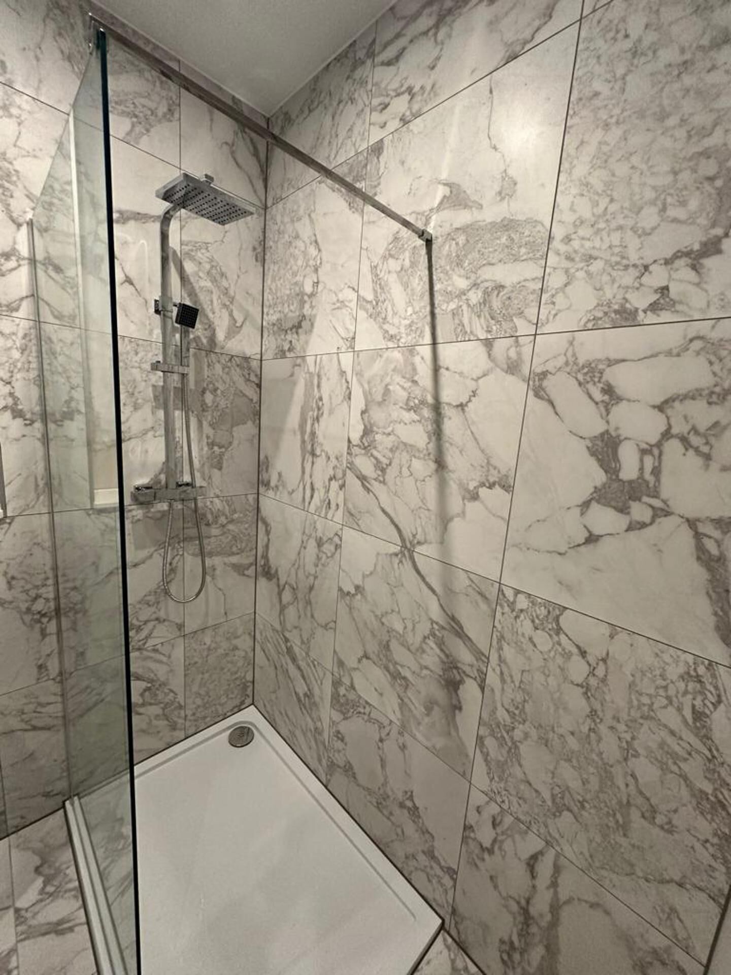 A shower with a glass door and marble tiles.