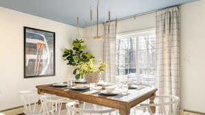 A dining area with a wooden table set for six, surrounded by white chairs, a large potted plant, and a chandelier. - Walk to Beach HotTub FirePit Game room Lake View (East Stroudsburg)