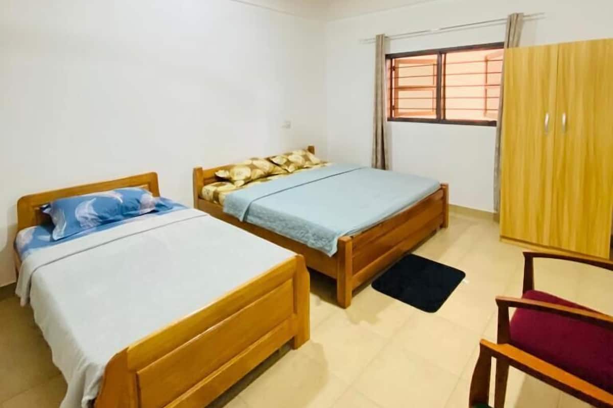 A room with two wooden beds, a ceiling fan, a window with curtains, and a wardrobe.