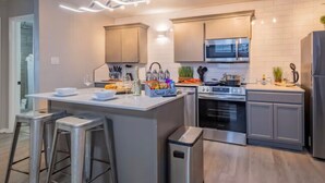 A modern kitchen with a central island, stainless steel appliances, and bar stools. - Beautiful Contemporary Suite #09 (Lawton)