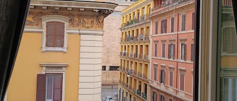 A street view with yellow and pink buildings, parked cars, and a clear sky.