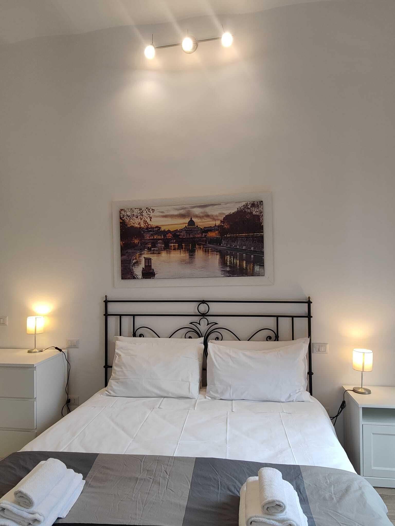 Quarto de hotel com cama, duas mesas de cabeceira, um quadro na parede e um lustre.