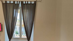 Un salon avec un canapé gris, un téléviseur à écran plat et une fenêtre ornée de rideaux gris.