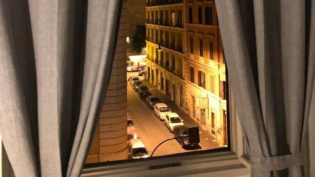Une vue à travers une fenêtre avec des rideaux, dévoilant une scène de rue avec des bâtiments et des voitures garées.