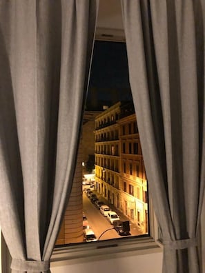 A view through a window with curtains, revealing a street scene with buildings and parked cars. - White King Rooms (Rome)