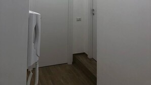 Un couloir étroit aux murs blancs et au plancher en bois. On y trouve deux portes blanches, dont l’une est ornée d’une serviette.