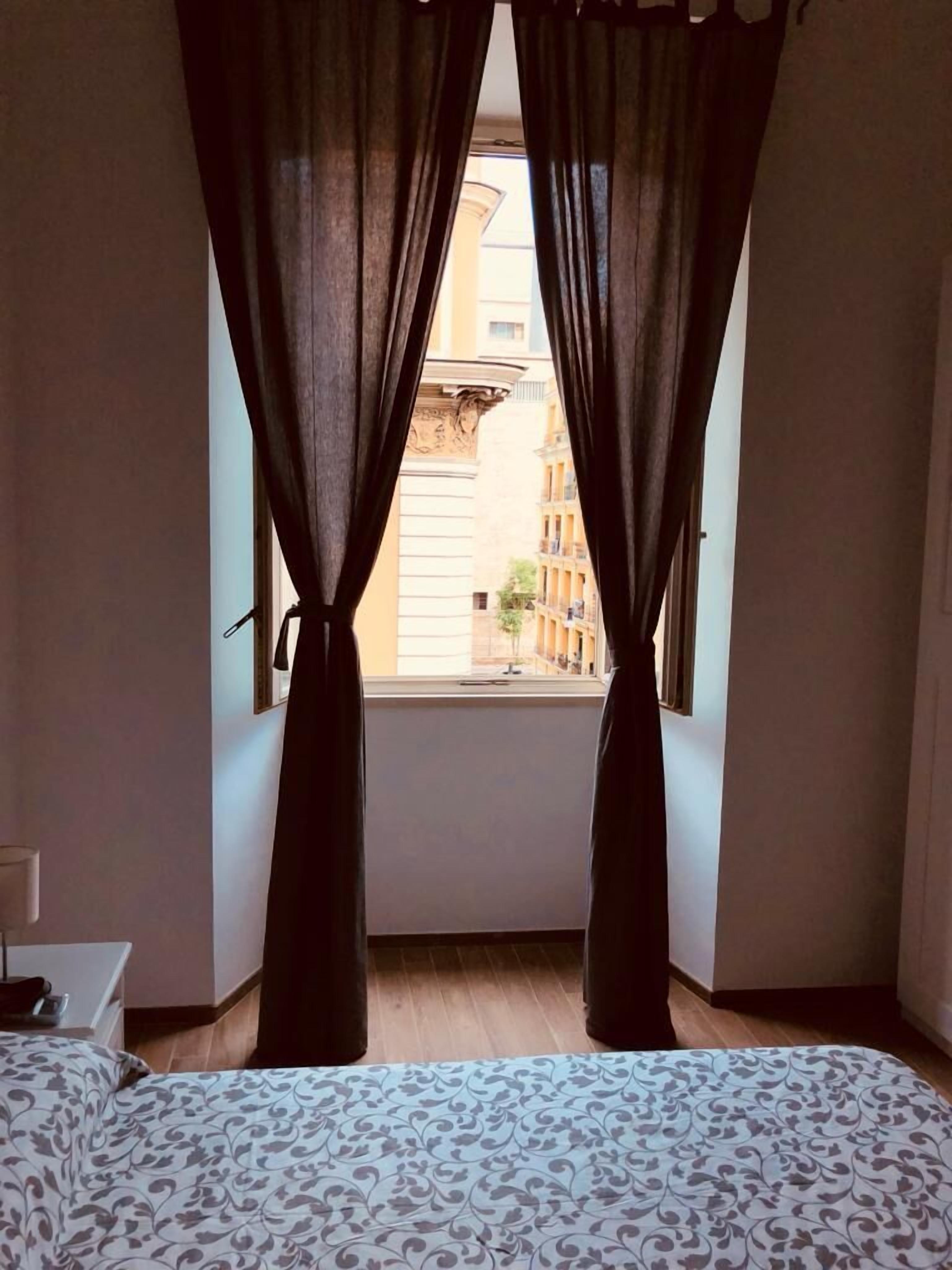 Une chambre à coucher avec un lit, une fenêtre avec des rideaux et une vue sur les bâtiments à l’extérieur.