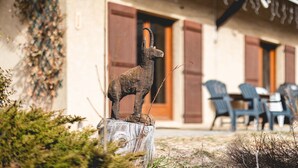 Un'area esterna rustica con una scultura in legno di un animale su un ceppo, un edificio con persiane in legno e posti a sedere all'aperto.