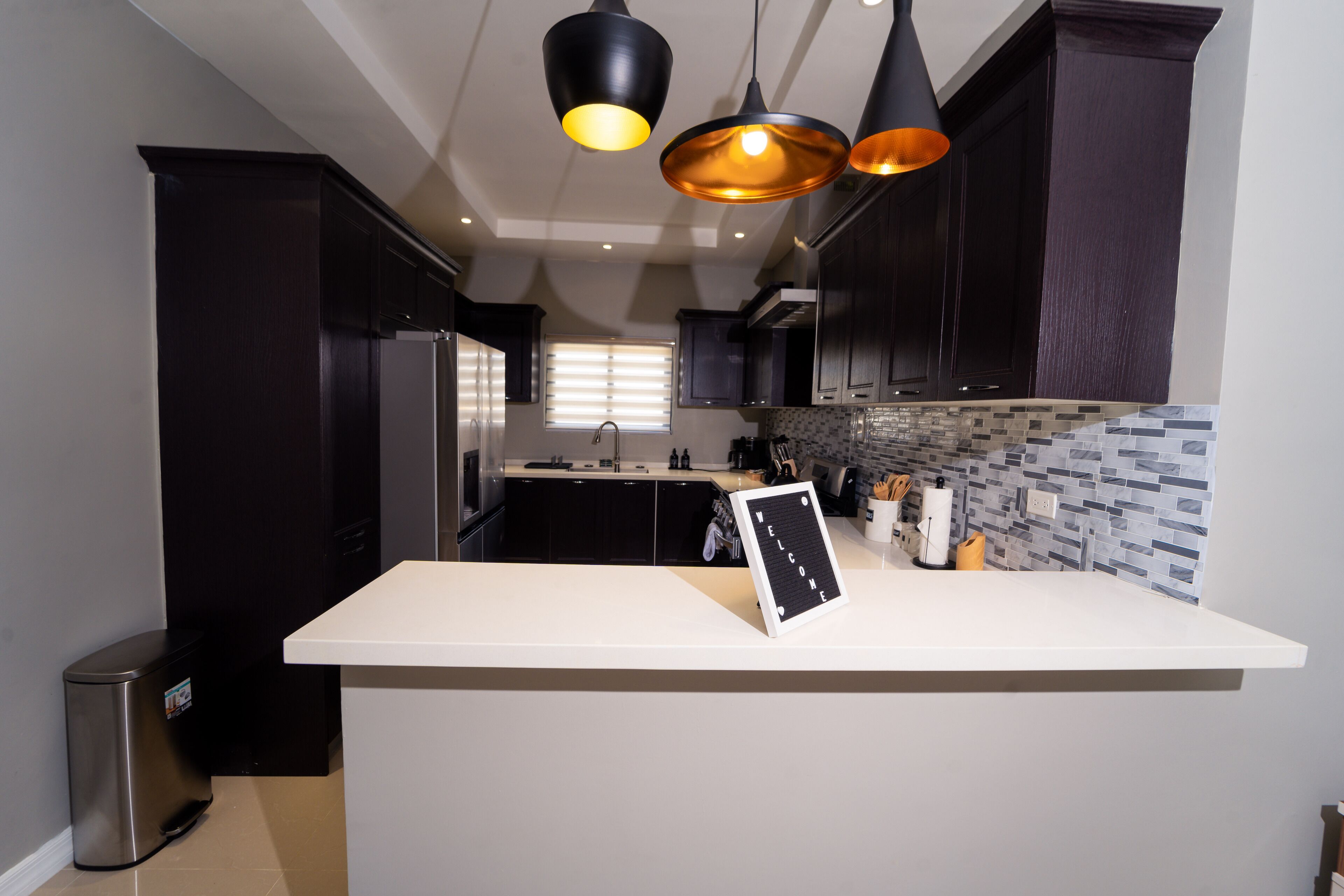 A modern kitchen with dark cabinets, a white countertop, and pendant lighting.