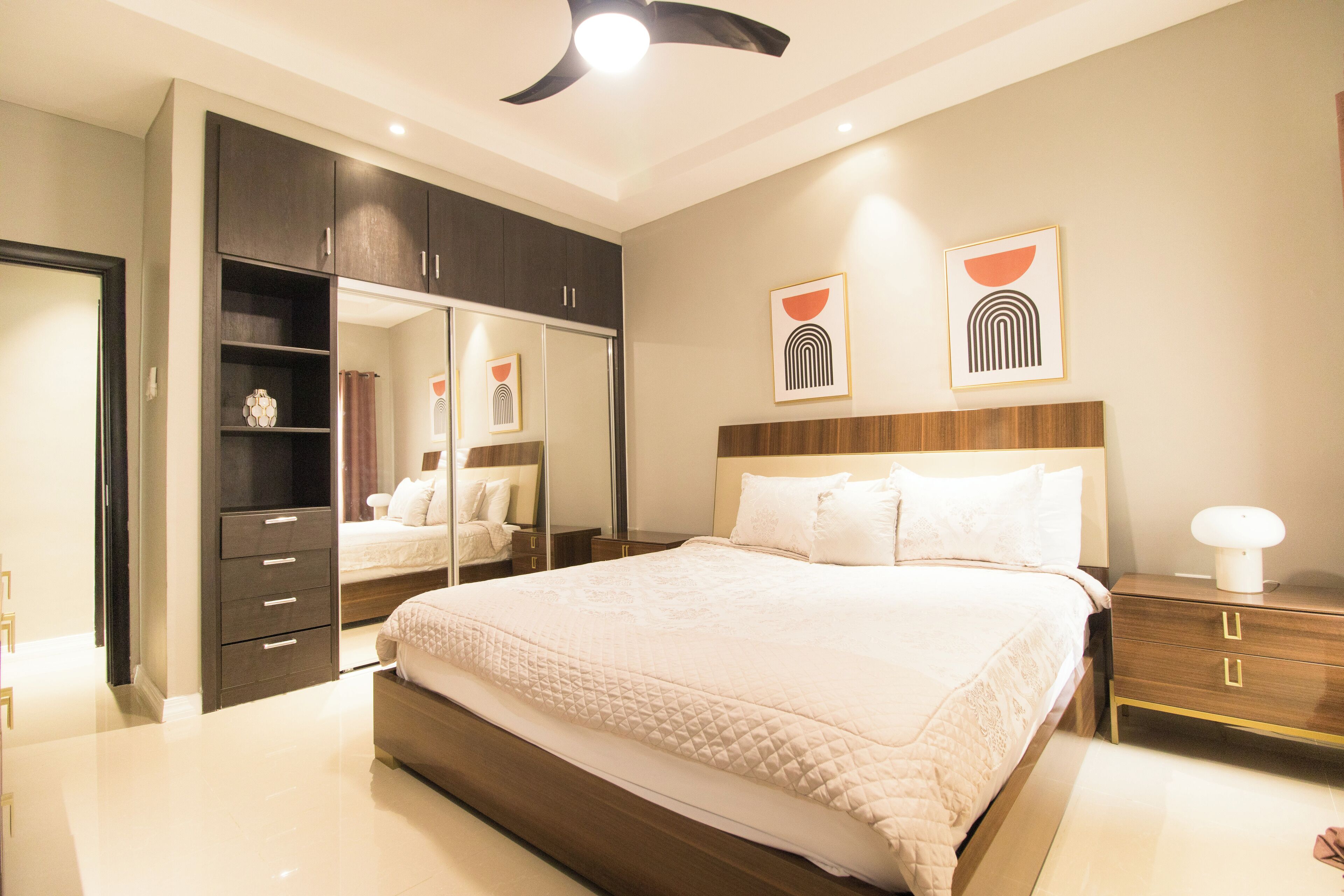 A modern bedroom with a large bed, dark wooden wardrobe, and bedside tables.