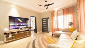A modern living room with a flat-screen TV, a ceiling fan, a sofa, and a large window with curtains. - LnD Villa! Lovely gated community, 24 hrs security, amazing view, and pool  (Ocho Rios)