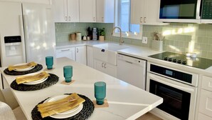 Une cuisine moderne avec des meubles blancs, un four à micro-ondes encastré, un lave-vaisselle et un grand îlot central agrémenté de verres et d’assiettes bleus.