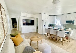 A modern kitchen with white cabinets, a built-in microwave, and a dining area with bar stools.