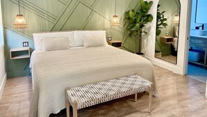 Une chambre à coucher comprenant un lit, des tables de chevet, un banc, un ventilateur de plafond et un grand miroir.