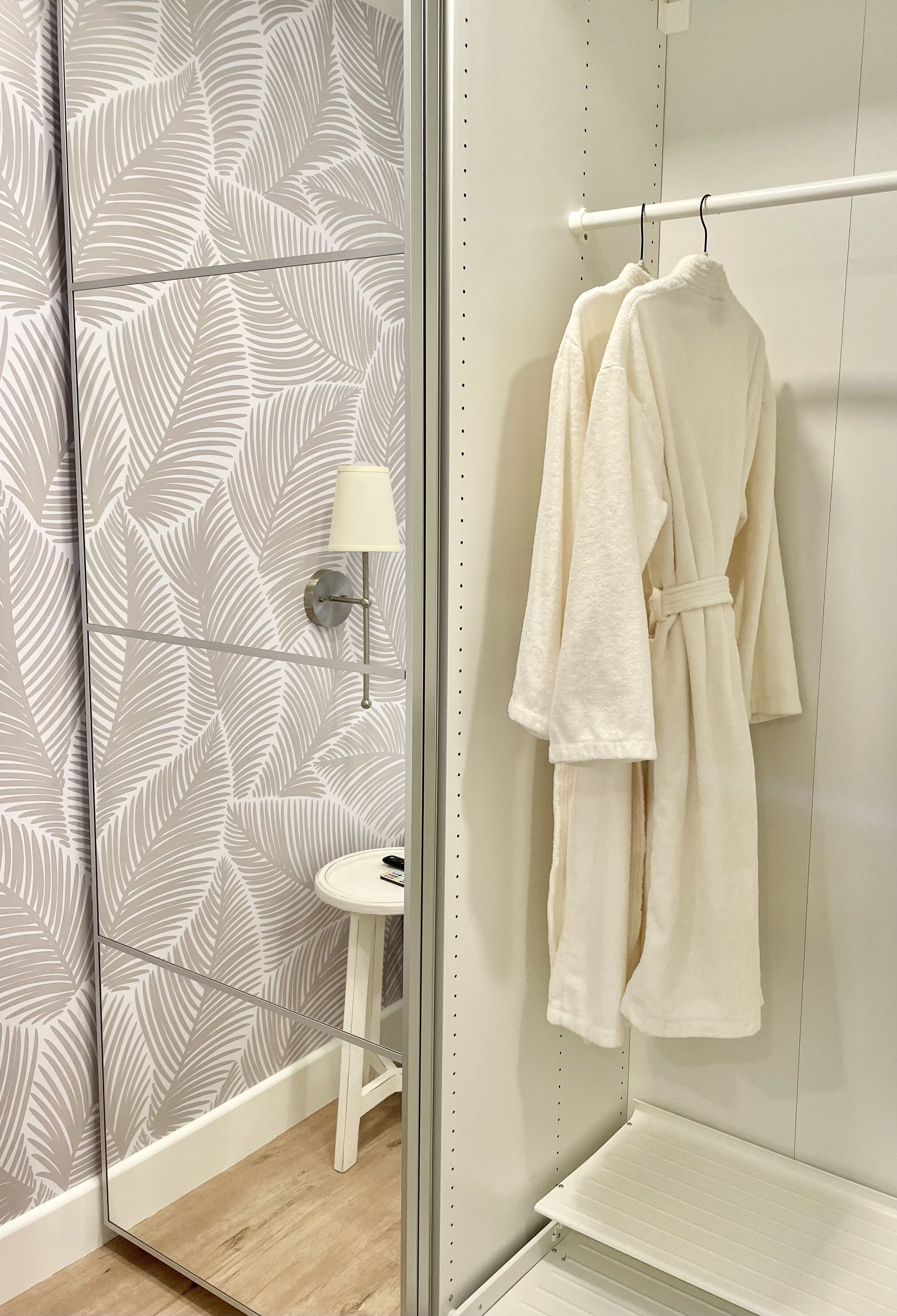 A bathroom with a mirror, a towel rack with a robe, and a wall with a leaf pattern.