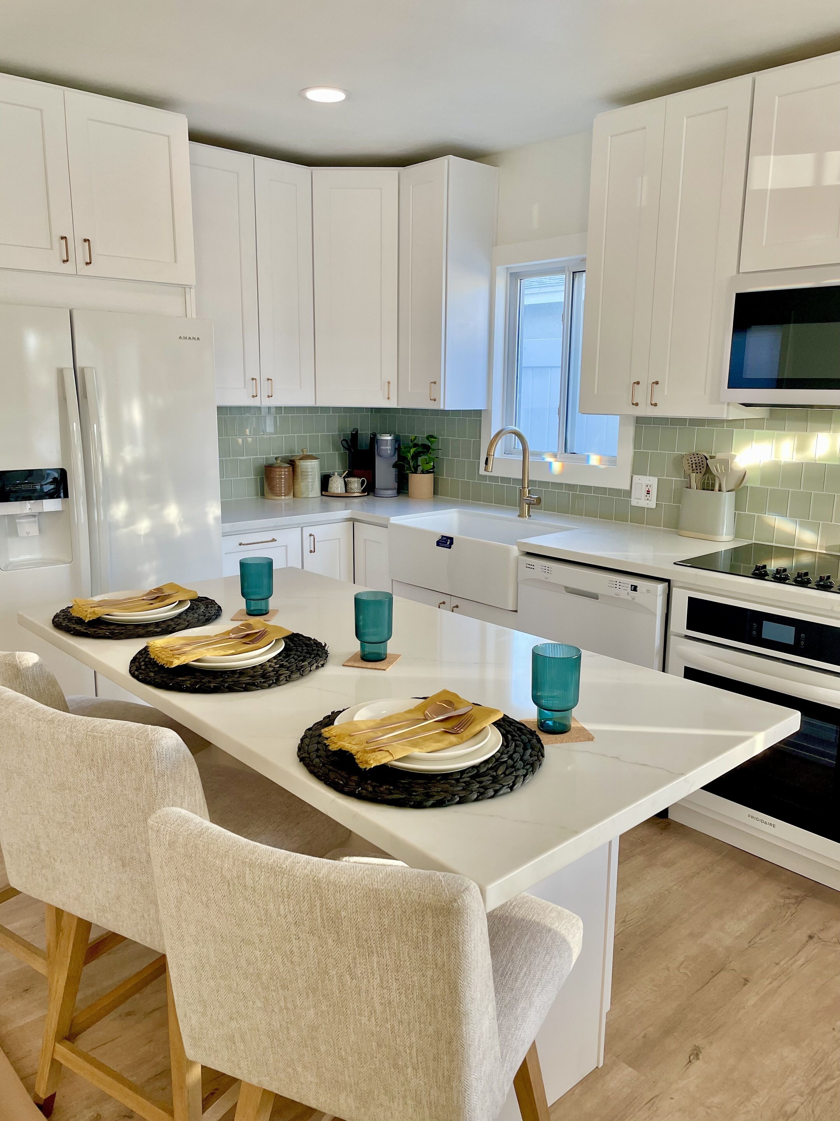 Una cocina moderna con armarios blancos, una isla central con un fregadero y un área de comedor con sillas y una mesa dispuesta para dos personas.