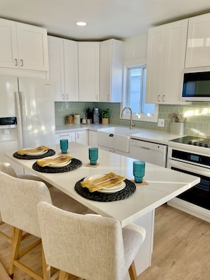 A modern kitchen with white cabinets, a central island with a sink, and a dining area with chairs and a table set for two.