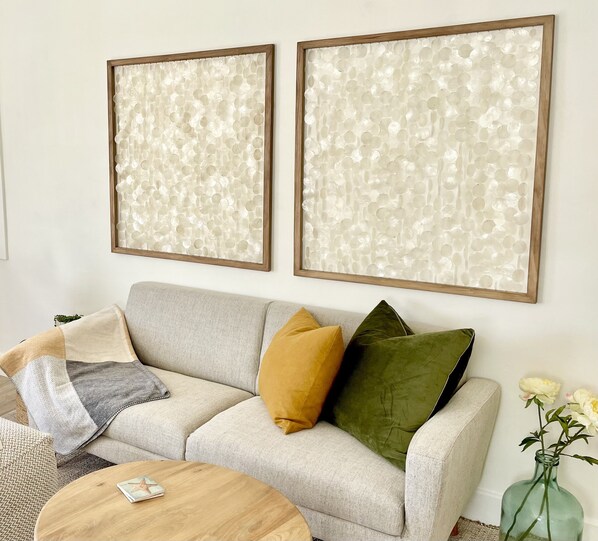 A living room with a sofa, two cushions, a small round table, and a vase with flowers.