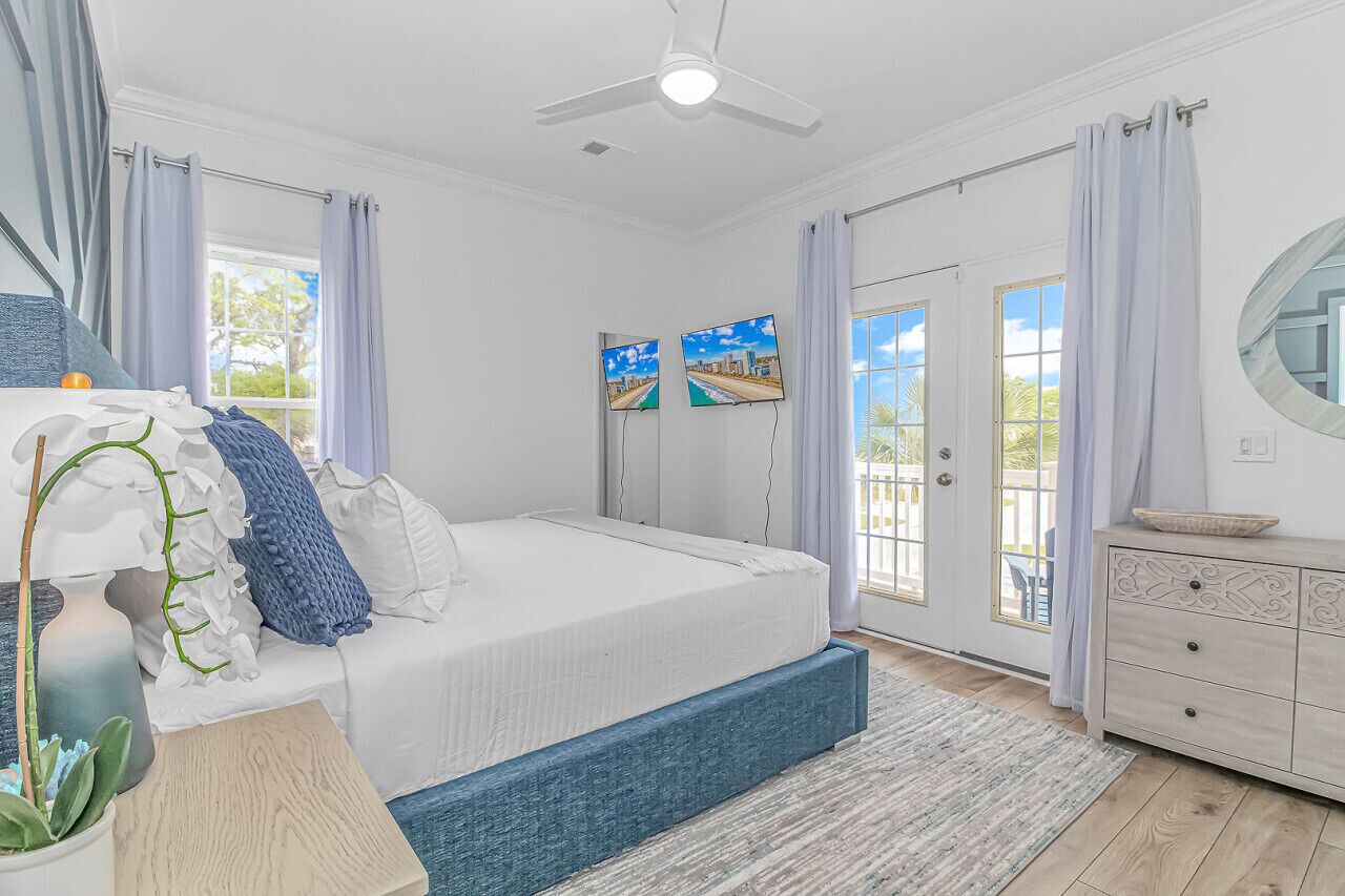 A bedroom with a bed, a dresser, a ceiling fan, and two wall-mounted TVs.