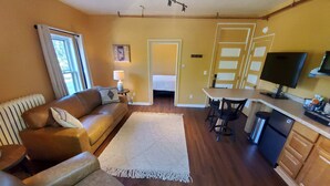 A cozy living room with a brown leather sofa, a white rug, and a dining area with a table and chairs. - Deluxe Queen with Park View (Laurium)