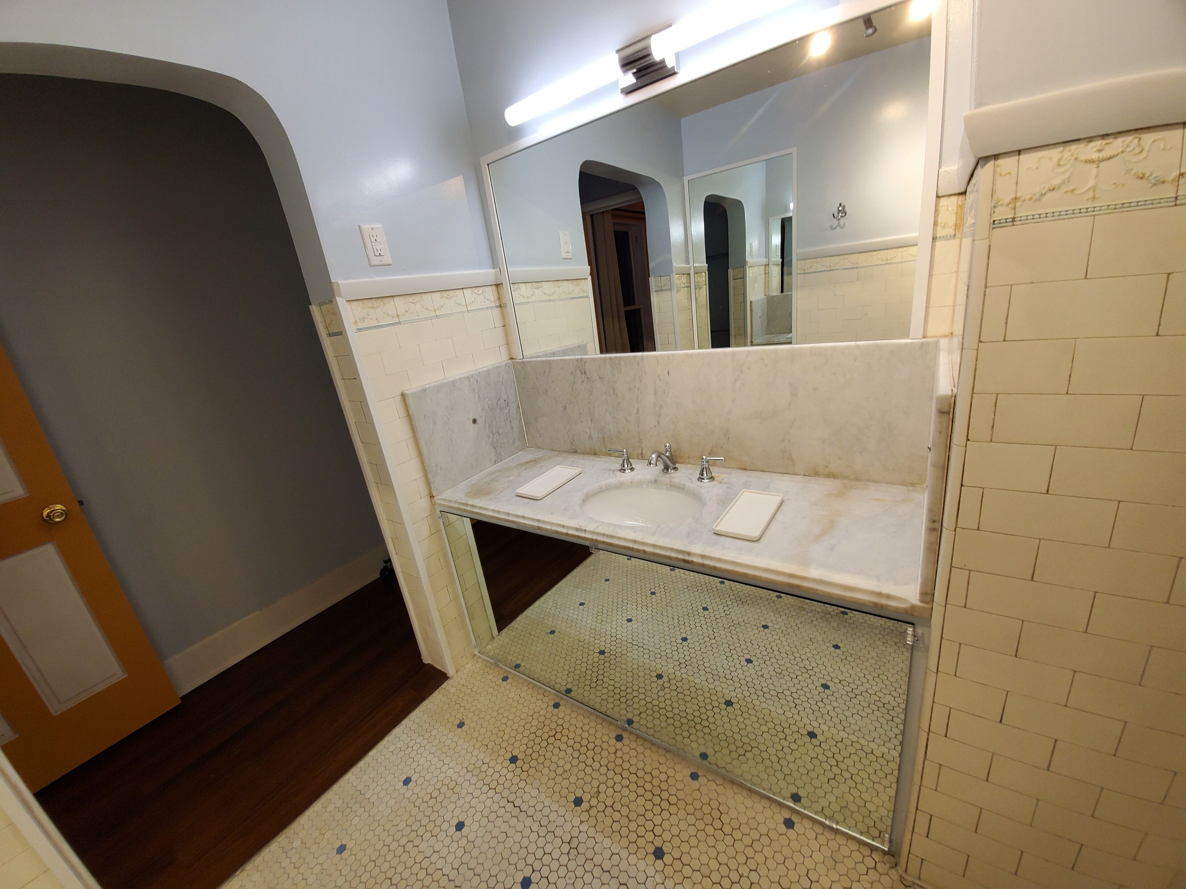Een badkamer met een wit wastafelmeubel, twee spiegels en een betegelde vloer.