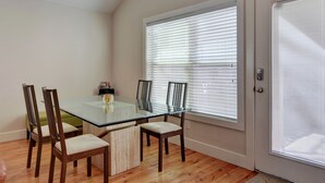 A dining area with a glass table, four wooden chairs, and a window with blinds.