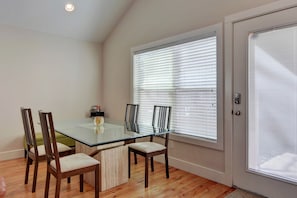 A dining area with a glass table, four wooden chairs, and a window with blinds.