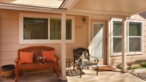 A covered porch with a wooden bench and a metal chair, a small table, and a potted plant.