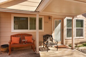 A covered porch with a wooden bench and a metal chair, a small table, and a potted plant.