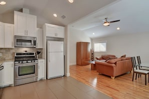 A modern kitchen with white cabinets, stainless steel appliances, and a wooden dining area with a sofa and chairs.