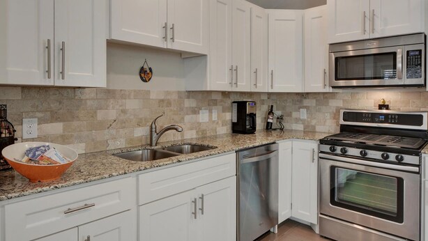 A modern kitchen with white cabinets, stainless steel appliances, a granite countertop, and a dish drying rack.