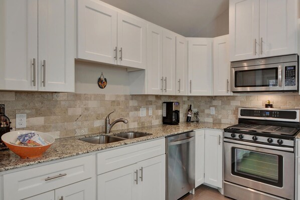 A modern kitchen with white cabinets, stainless steel appliances, a granite countertop, and a dish drying rack.