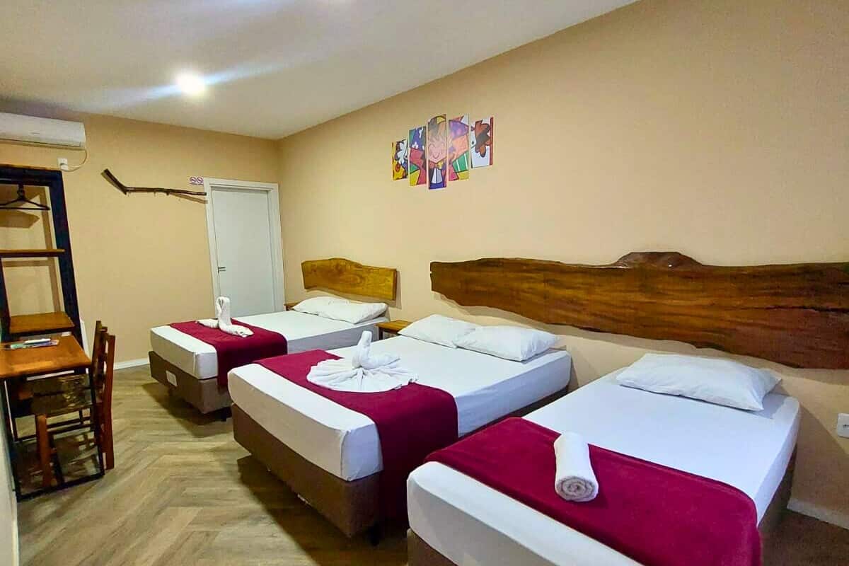 Une chambre d’hôtel avec trois lits simples, une tête de lit en bois, une petite table et une chaise.
