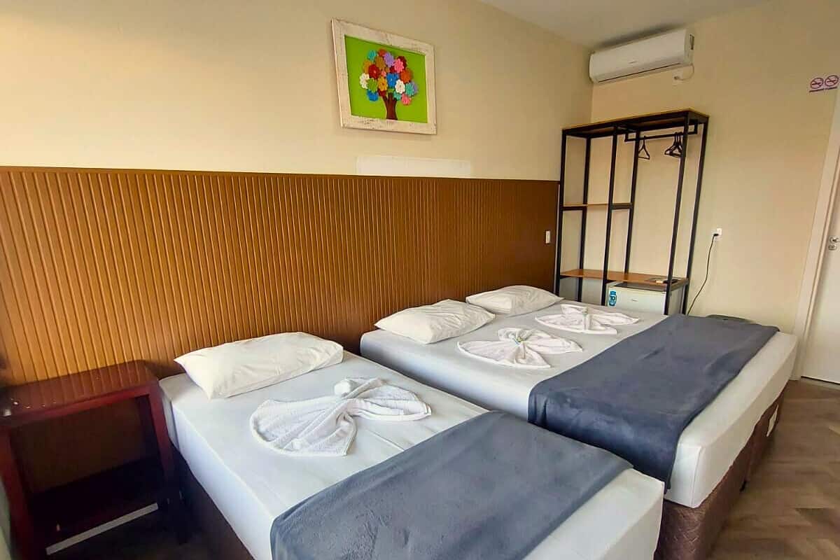 Une chambre d’hôtel avec deux lits, une tête de lit en bois, un climatiseur fixé au mur et un tableau coloré au-dessus des lits.