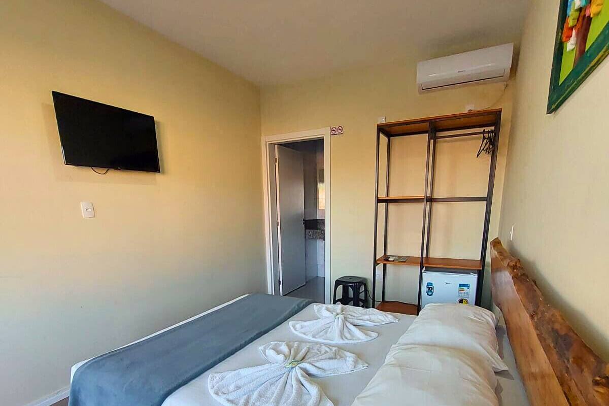 Une chambre d’hôtel avec un lit, un téléviseur fixé au mur, une tête de lit en bois et une petite étagère.