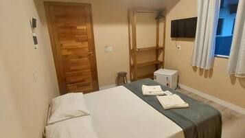 Un dormitorio con cama, una puerta de madera, televisor y ventana con cortinas.
