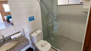 A modern bathroom with a glass shower enclosure, a white toilet, a granite countertop sink, and a visible trash bin.