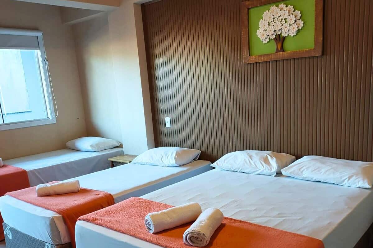Une chambre d’hôtel avec deux lits, chacun doté d’un matelas blanc et de couvertures orange, ainsi que d’une tête de lit en bois.