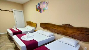 A hotel room with three single beds, each with a wooden headboard, white bedding, and a red throw blanket.