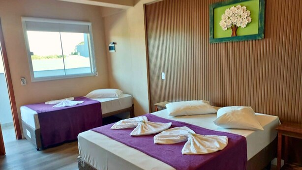 A hotel room with two beds, a window, a wall-mounted picture, and a wooden floor.