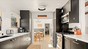 Une cuisine moderne avec des meubles de couleur sombre, un îlot central et un coin repas comprenant une table et des chaises en bois.