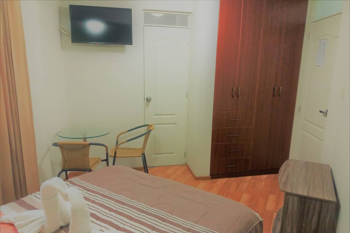 A bedroom with a bed, a television, a wardrobe, and a small table with chairs.