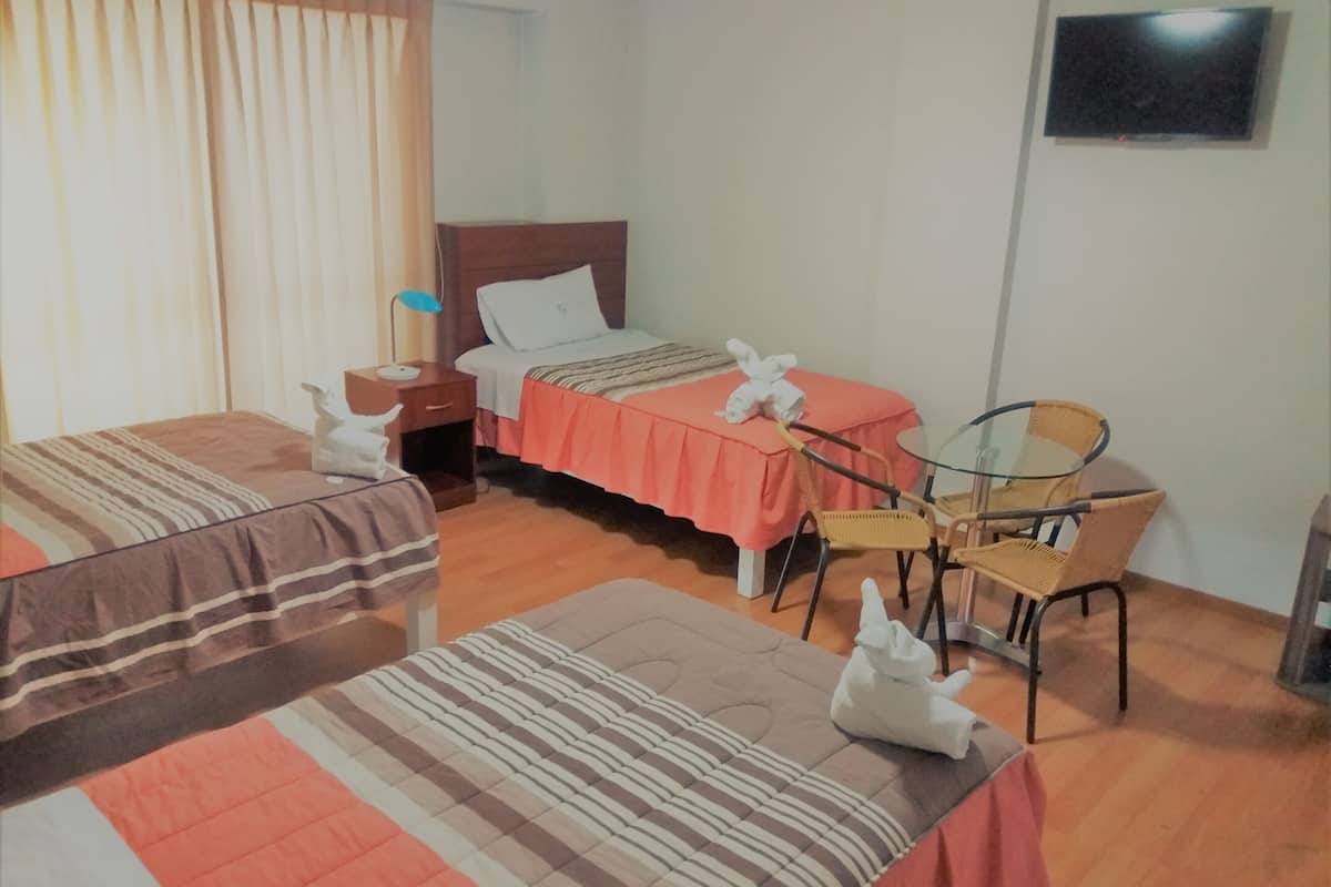 A hotel room with two single beds, a small table with chairs, a nightstand, and a television on the wall.
